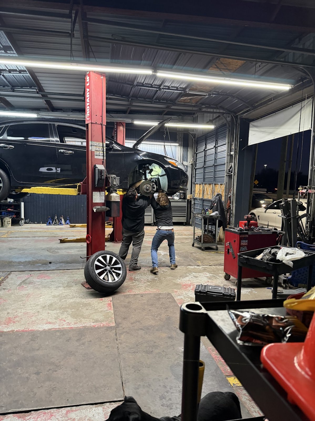 Technicians performing brake and suspension work on a lifted vehicle